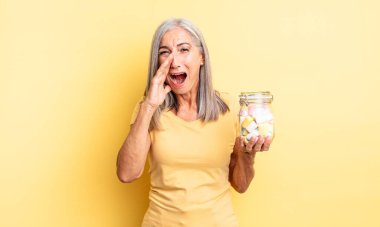 Orta yaşlı, güzel bir kadın kendini mutlu hissediyor. Elleri ağzının kenarında bağırıyor. Şeker şişesi konsepti