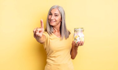 Orta yaşlı güzel bir kadın gülümsüyor ve arkadaş canlısı görünüyor. Bir numarayı gösteriyor. Şeker şişesi konsepti