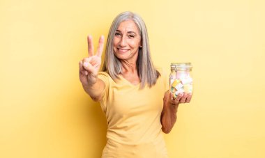 Orta yaşlı güzel bir kadın gülümsüyor ve arkadaş canlısı görünüyor. İki numarayı gösteriyor. Şeker şişesi konsepti