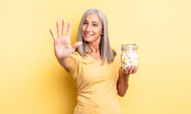 Orta yaşlı güzel bir kadın gülümsüyor ve arkadaş canlısı görünüyor, beş numarayı gösteriyor. Şeker şişesi konsepti