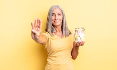 Orta yaşlı güzel bir kadın gülümsüyor ve arkadaş canlısı görünüyor, dört numarayı gösteriyor. Şeker şişesi konsepti