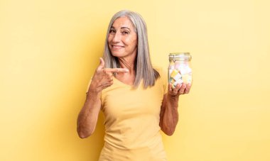 Orta yaşlı güzel bir kadın neşeli bir şekilde gülümsüyor, mutlu hissediyor ve bir tarafı işaret ediyor. Şeker şişesi konsepti