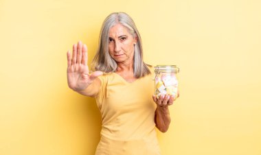 Orta yaşlı, güzel bir kadın ciddi görünüyor. Avuç içini gösteriyor. Durdurma hareketi yapıyor. Şeker şişesi konsepti