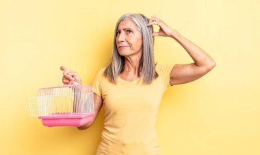 Orta yaşlı, güzel bir kadın şaşkın ve kafası karışık, kaşınıyor. evcil hayvan kafesi veya hapishane konsepti