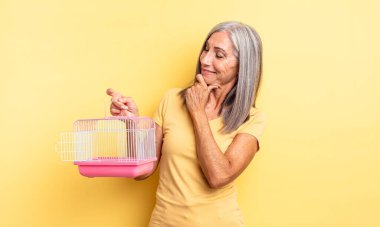 Orta yaşlı güzel bir kadın mutlu, kendinden emin ve elleri çenesinde gülümsüyor. evcil hayvan kafesi veya hapishane konsepti