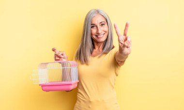 Orta yaşlı güzel bir kadın gülümsüyor ve mutlu görünüyor, zafer ya da barış işareti yapıyor. evcil hayvan kafesi veya hapishane konsepti