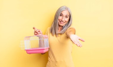 Orta yaşlı, güzel bir kadın arkadaşça gülümsüyor ve bir konsept sunuyor. evcil hayvan kafesi veya hapishane konsepti