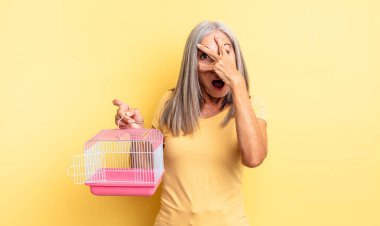 Orta yaşlı, güzel bir kadın şok olmuş, korkmuş ya da korkmuş görünüyor, yüzünü elleriyle kapatıyor. evcil hayvan kafesi veya hapishane konsepti
