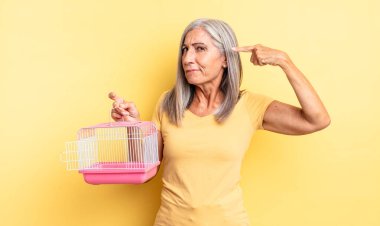 Orta yaşlı güzel bir kadın kafası karışık ve şaşkın hissediyor, deli olduğunu gösteriyor. evcil hayvan kafesi veya hapishane konsepti