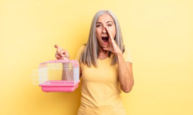 Orta yaşlı, güzel bir kadın kendini mutlu hissediyor. Elleri ağzının kenarında bağırıyor. evcil hayvan kafesi veya hapishane konsepti