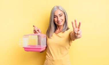Orta yaşlı güzel bir kadın gülümsüyor ve arkadaş canlısı görünüyor, üç numarayı gösteriyor. evcil hayvan kafesi veya hapishane konsepti