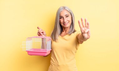 Orta yaşlı güzel bir kadın gülümsüyor ve arkadaş canlısı görünüyor, dört numarayı gösteriyor. evcil hayvan kafesi veya hapishane konsepti