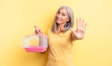 Orta yaşlı güzel bir kadın gülümsüyor ve arkadaş canlısı görünüyor, beş numarayı gösteriyor. evcil hayvan kafesi veya hapishane konsepti
