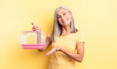 Orta yaşlı güzel bir kadın neşeli bir şekilde gülümsüyor, mutlu hissediyor ve bir konsept gösteriyor. evcil hayvan kafesi veya hapishane konsepti