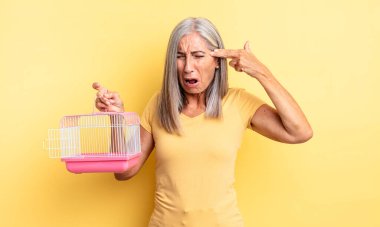 Orta yaşlı, güzel bir kadın mutsuz ve stresli görünüyor, intihar jesti silah işareti yapıyor. evcil hayvan kafesi veya hapishane konsepti