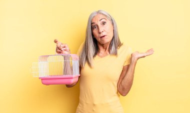 Orta yaşlı, güzel bir kadın şaşırmış ve şok olmuş görünüyor. Çenesi düşmüş ve elinde bir nesne var. evcil hayvan kafesi veya hapishane konsepti