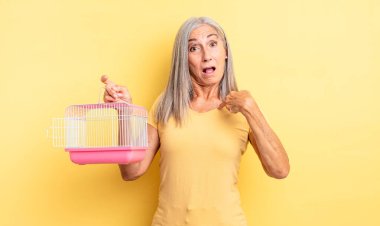 Orta yaşlı güzel bir kadın şok olmuş ve ağzı açık, kendini işaret eden bir şekilde şaşırmış görünüyor. evcil hayvan kafesi veya hapishane konsepti