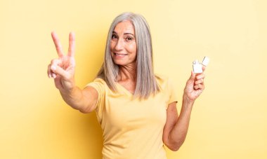 Orta yaşlı güzel bir kadın gülümsüyor ve mutlu görünüyor, zafer ya da barış işareti yapıyor. daha hafif kavram