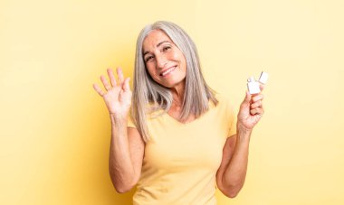 Orta yaşlı, güzel bir kadın mutlu bir şekilde gülümsüyor, el sallıyor, sizi selamlıyor. daha hafif kavram