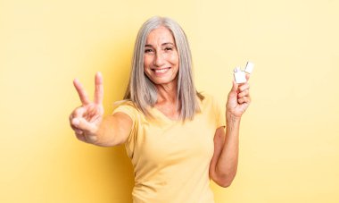 Orta yaşlı güzel bir kadın gülümsüyor ve arkadaş canlısı görünüyor. İki numarayı gösteriyor. daha hafif kavram