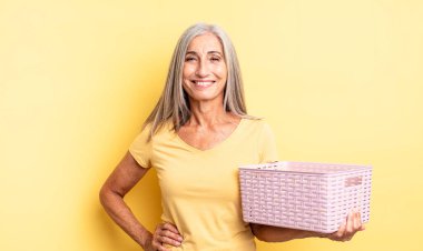 Orta yaşlı güzel bir kadın mutlu bir şekilde gülümsüyor, eli kalçasında ve kendinden emin. boş sepet konsepti