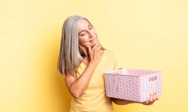 Orta yaşlı güzel bir kadın mutlu, kendinden emin ve elleri çenesinde gülümsüyor. boş sepet konsepti