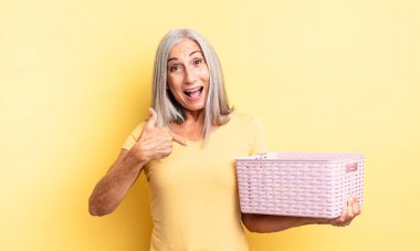 Orta yaşlı, güzel bir kadın kendini mutlu hissediyor ve heyecanla kendini işaret ediyor. boş sepet konsepti
