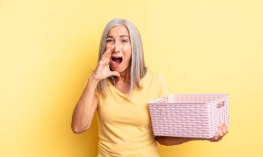 Orta yaşlı, güzel bir kadın kendini mutlu hissediyor. Elleri ağzının kenarında bağırıyor. boş sepet konsepti