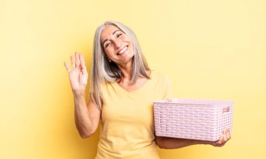 Orta yaşlı, güzel bir kadın mutlu bir şekilde gülümsüyor, el sallıyor, sizi selamlıyor. boş sepet konsepti