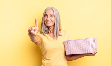 Orta yaşlı güzel bir kadın gülümsüyor ve arkadaş canlısı görünüyor. Bir numarayı gösteriyor. boş sepet konsepti