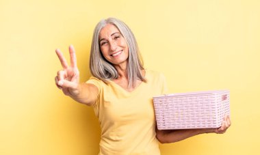 Orta yaşlı güzel bir kadın gülümsüyor ve arkadaş canlısı görünüyor. İki numarayı gösteriyor. boş sepet konsepti