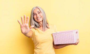 Orta yaşlı güzel bir kadın gülümsüyor ve arkadaş canlısı görünüyor, beş numarayı gösteriyor. boş sepet konsepti