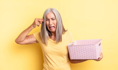Orta yaşlı, güzel bir kadın mutsuz ve stresli görünüyor, intihar jesti silah işareti yapıyor. boş sepet konsepti