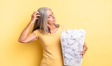 Orta yaşlı, güzel bir kadın şaşkın ve kafası karışık, kaşınıyor. kağıt toplar başarısızlık konsepti