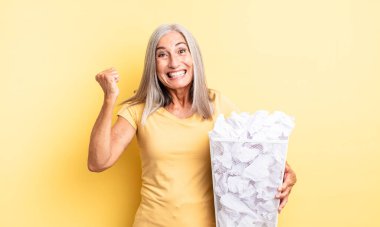 Orta yaşlı, güzel bir kadın şokta, gülüyor ve başarıyı kutluyor. kağıt toplar başarısızlık konsepti