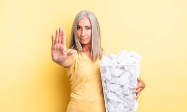 Orta yaşlı, güzel bir kadın ciddi görünüyor. Avuç içini gösteriyor. Durdurma hareketi yapıyor. kağıt toplar başarısızlık konsepti