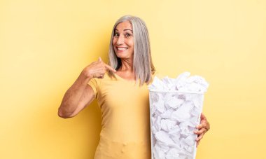 Orta yaşlı, güzel bir kadın kendini mutlu hissediyor ve heyecanla kendini işaret ediyor. kağıt toplar başarısızlık konsepti