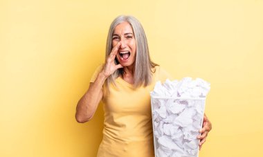 Orta yaşlı, güzel bir kadın kendini mutlu hissediyor. Elleri ağzının kenarında bağırıyor. kağıt toplar başarısızlık konsepti