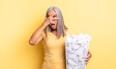 Orta yaşlı, güzel bir kadın şok olmuş, korkmuş ya da korkmuş görünüyor, yüzünü elleriyle kapatıyor. kağıt toplar başarısızlık konsepti