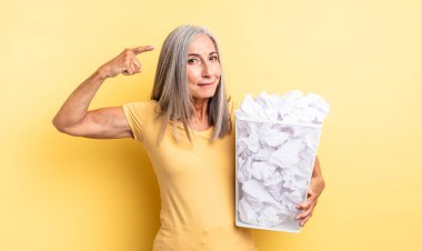 Orta yaşlı güzel bir kadın kafası karışık ve şaşkın hissediyor, deli olduğunu gösteriyor. kağıt toplar başarısızlık konsepti