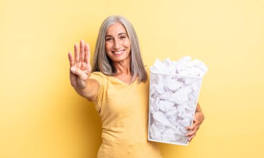 Orta yaşlı güzel bir kadın gülümsüyor ve arkadaş canlısı görünüyor, dört numarayı gösteriyor. kağıt toplar başarısızlık konsepti