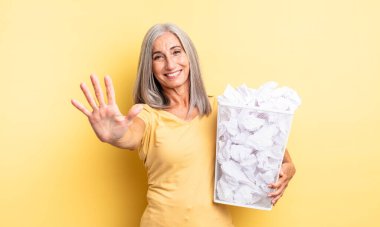 Orta yaşlı güzel bir kadın gülümsüyor ve arkadaş canlısı görünüyor, beş numarayı gösteriyor. kağıt toplar başarısızlık konsepti