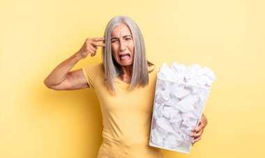 Orta yaşlı, güzel bir kadın mutsuz ve stresli görünüyor, intihar jesti silah işareti yapıyor. kağıt toplar başarısızlık konsepti