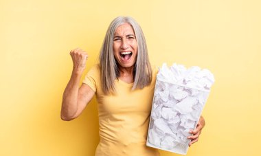 Orta yaşlı, güzel bir kadın sinirli bir ifadeyle agresif bir şekilde bağırıyor. kağıt toplar başarısızlık konsepti