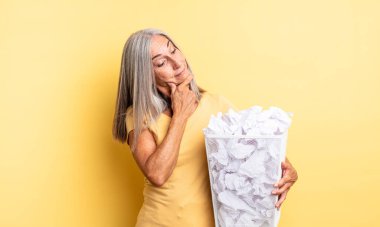 Orta yaşlı güzel bir kadın mutlu, kendinden emin ve elleri çenesinde gülümsüyor. kağıt toplar başarısızlık konsepti