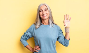 Orta yaşlı güzel bir kadın mutlu bir şekilde gülümsüyor, eli kalçasında ve kendinden emin. el bandajı konsepti