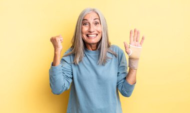 Orta yaşlı, güzel bir kadın şokta, gülüyor ve başarıyı kutluyor. el bandajı konsepti