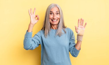 Orta yaşlı, güzel bir kadın kendini mutlu hissediyor, iyi bir jestle onaylıyor. el bandajı konsepti