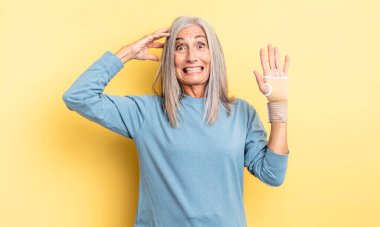 Orta yaşlı, güzel bir kadın stresli, endişeli ya da korkmuş, elleri başının üstünde. el bandajı konsepti