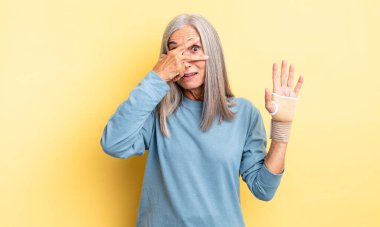 Orta yaşlı, güzel bir kadın şok olmuş, korkmuş ya da korkmuş görünüyor, yüzünü elleriyle kapatıyor. el bandajı konsepti